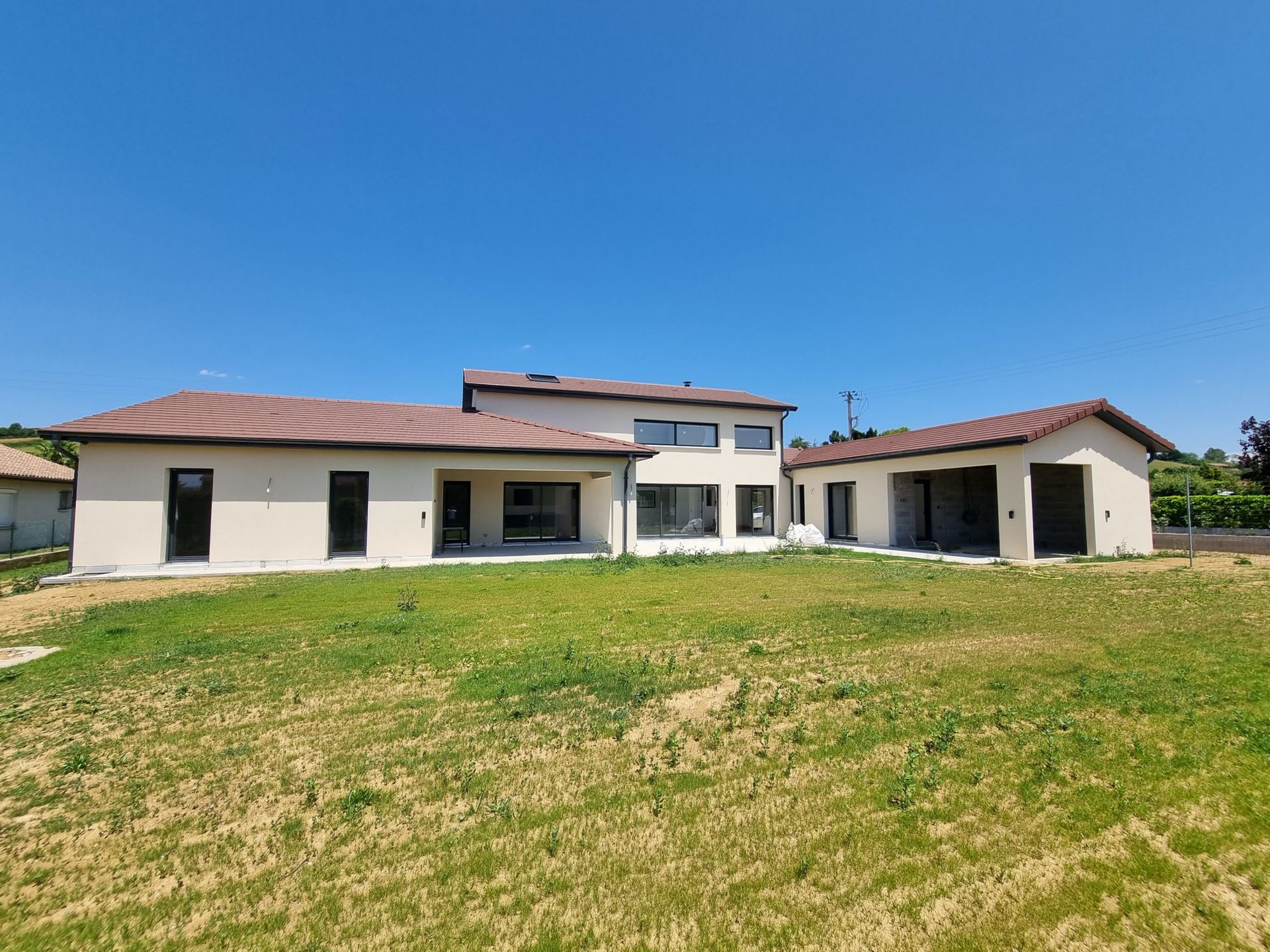 Nouvelle maison beige avec toits plats sur une pelouse verte sous un ciel bleu.