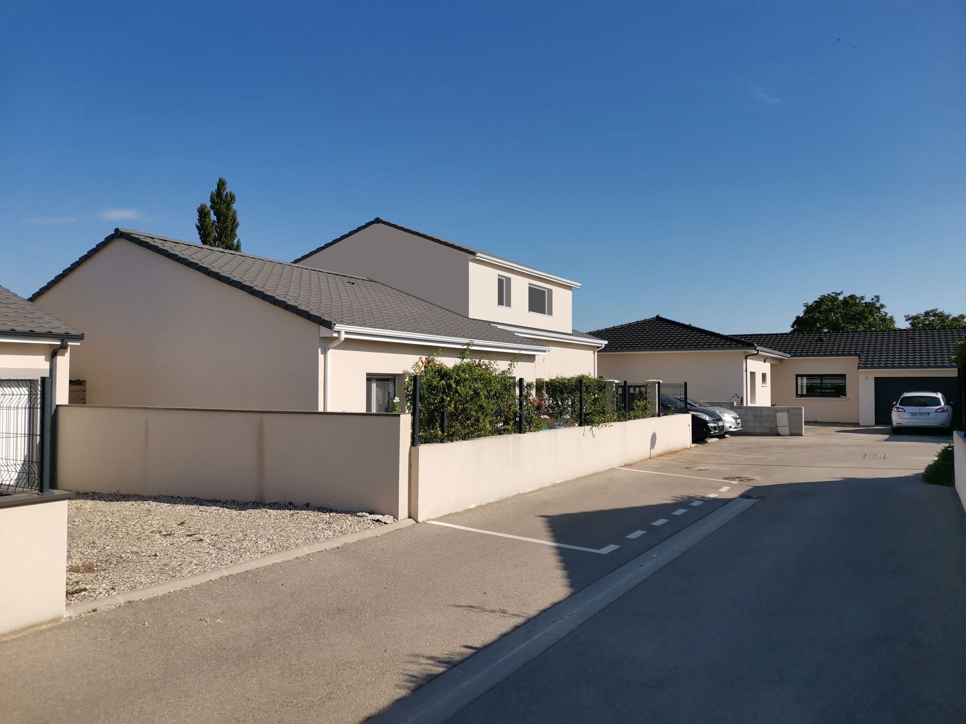 Rangée de maisons modernes aux murs clairs, aux toits gris et une rue pavée sous un ciel bleu.