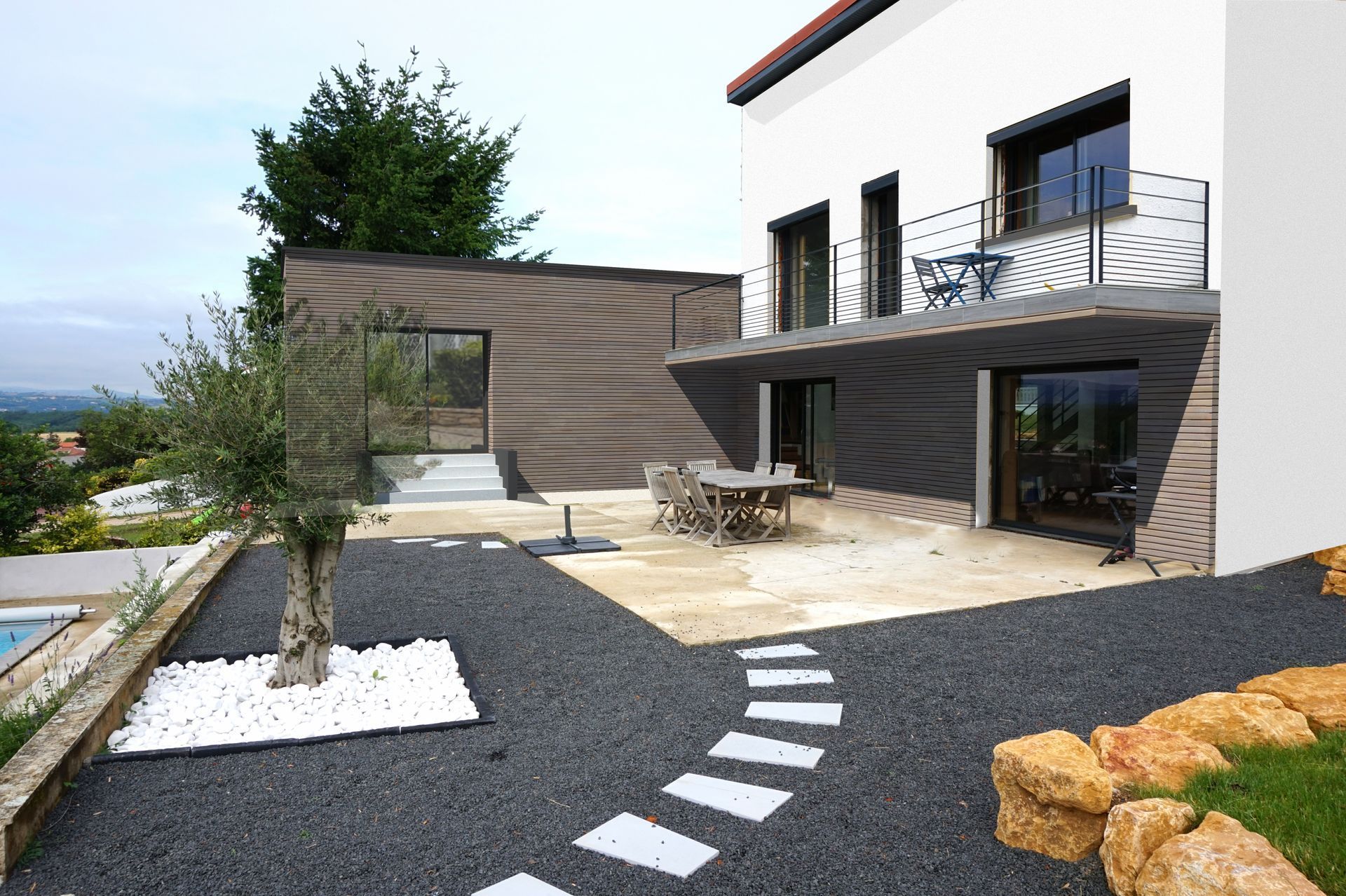 Voiture grise garée devant une maison beige clair avec une allée de gravier sous un ciel nuageux.