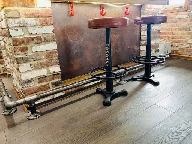 Zwei Barhocker stehen neben einer Backsteinwand in einem Raum.