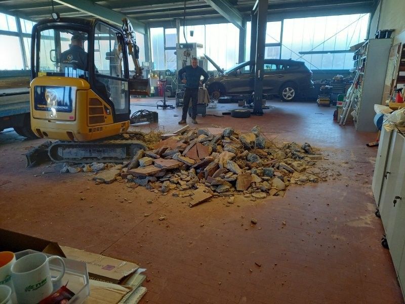 Gelber Bagger und Mann in einer Garage mit einem Schutthaufen auf rotem Boden.
