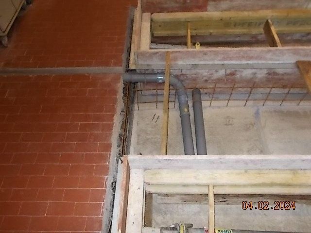 Baustelle mit freiliegenden Rohren, Ziegelmauer und Holzkonstruktion.