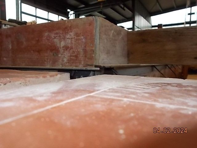 Nahaufnahme von roten Ziegelsteinen und Holzblöcken. Staub bedeckt die Oberfläche, möglicherweise in einer Werkstattumgebung.