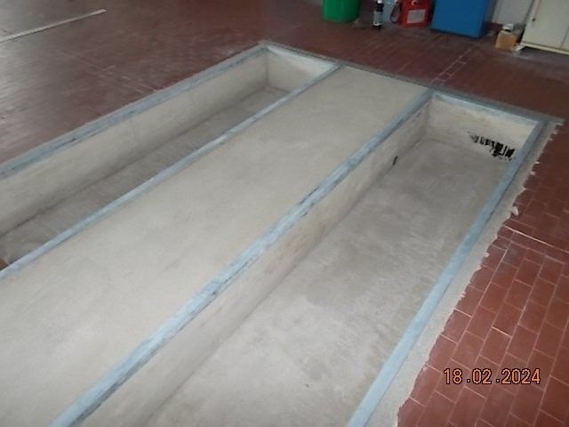 Eine lange, rechteckige Inspektionsgrube im Garagenboden, die mit Beton ausgekleidet ist.