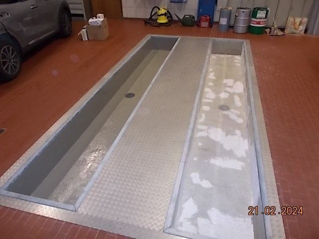 Eine leere Autowerkstattgrube. Graue Metallwände und -boden, roter Boden ringsum.