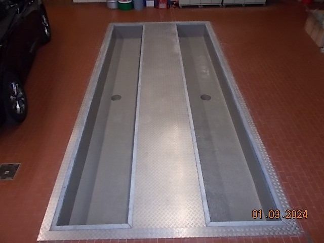 Eine rechteckige Inspektionsgrube für Kraftfahrzeuge mit Riffelblechboden in einer Garage.