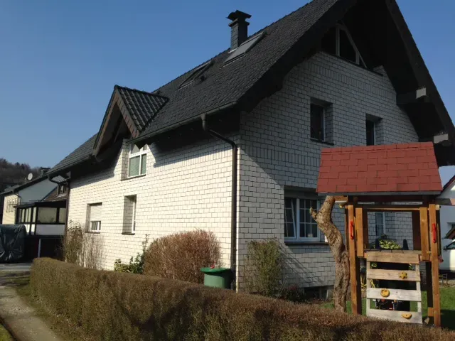 Ein weißes Backsteinhaus mit rotem Dach und einem Spielplatz davor
