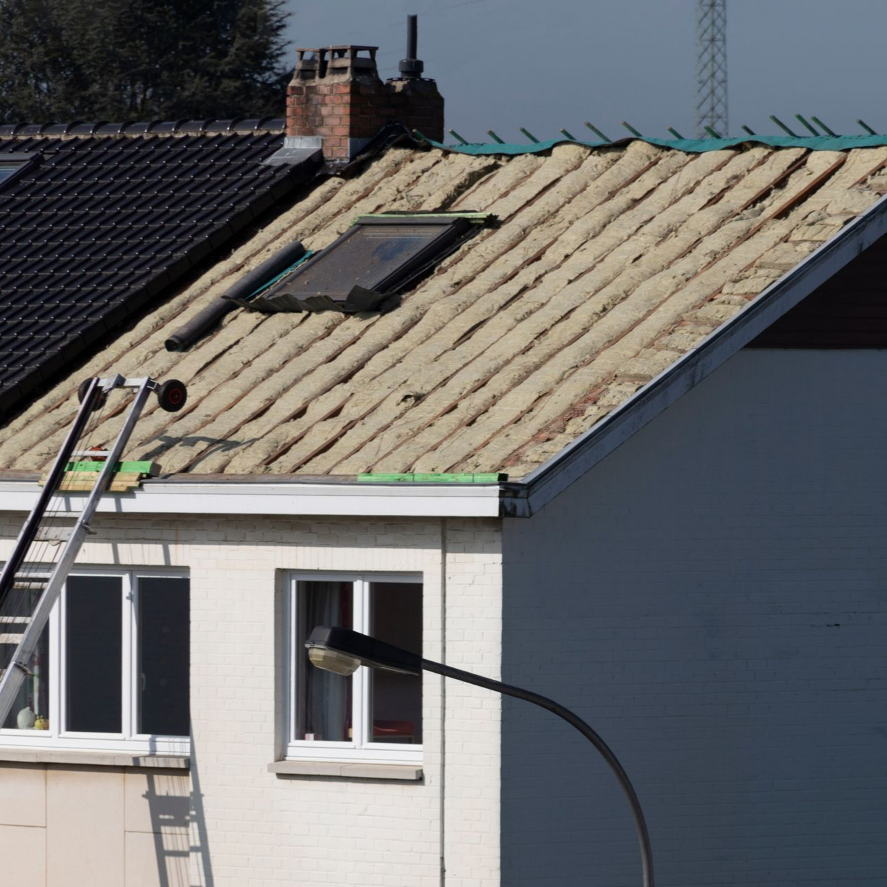 Réparation du toit d'une maison blanche, isolation beige et échelles visibles.