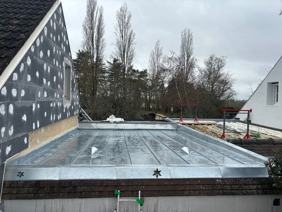 Toit plat en construction avec solins métalliques, bordure en briques et murs de maison en échafaudage à proximité.