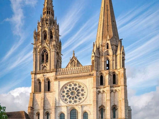 Façade de cathédrale avec deux flèches jumelles, une rosace et des arcades de pierre se détachant sur un ciel bleu.