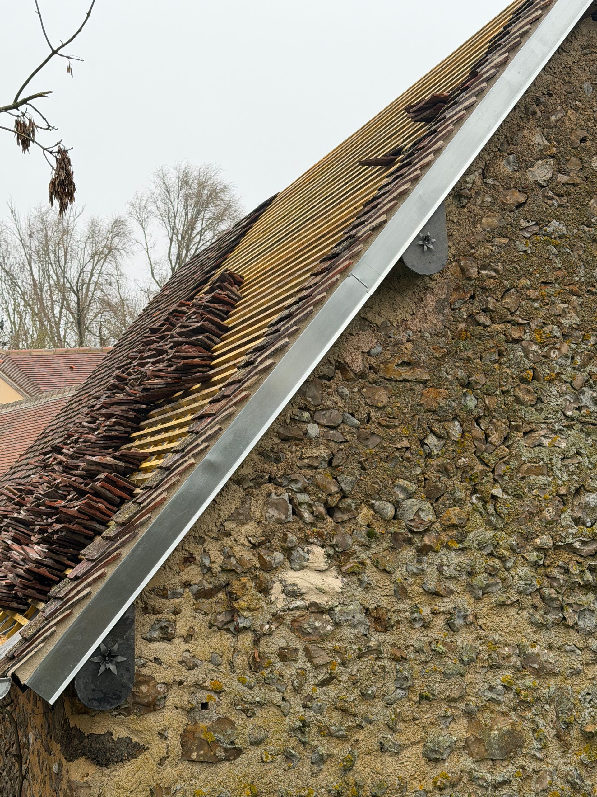 Gros plan sur un toit pentu où des feuilles mortes et des débris s'accumulent dans la gouttière.
