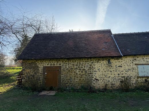 Maison en pierre avec un toit de chaume sombre et une porte en bois dans un cadre rural ensoleillé.