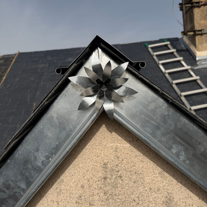 Faîtière métallique avec un chapeau de ventilation décoratif à côté d'une échelle sur le toit d'un bâtiment.