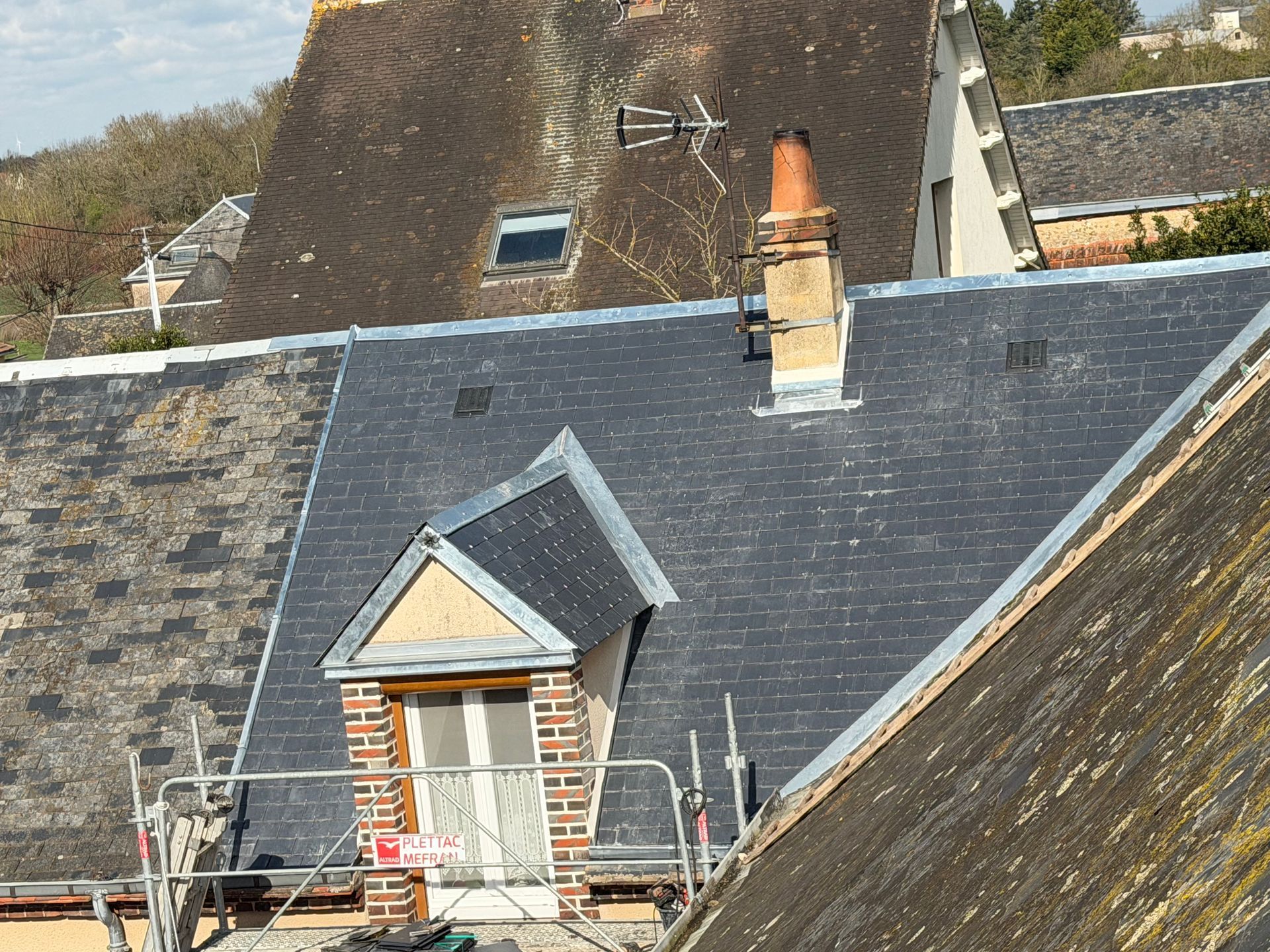 Toiture en ardoise sombre, lucarne, cheminée et échelle au bord.