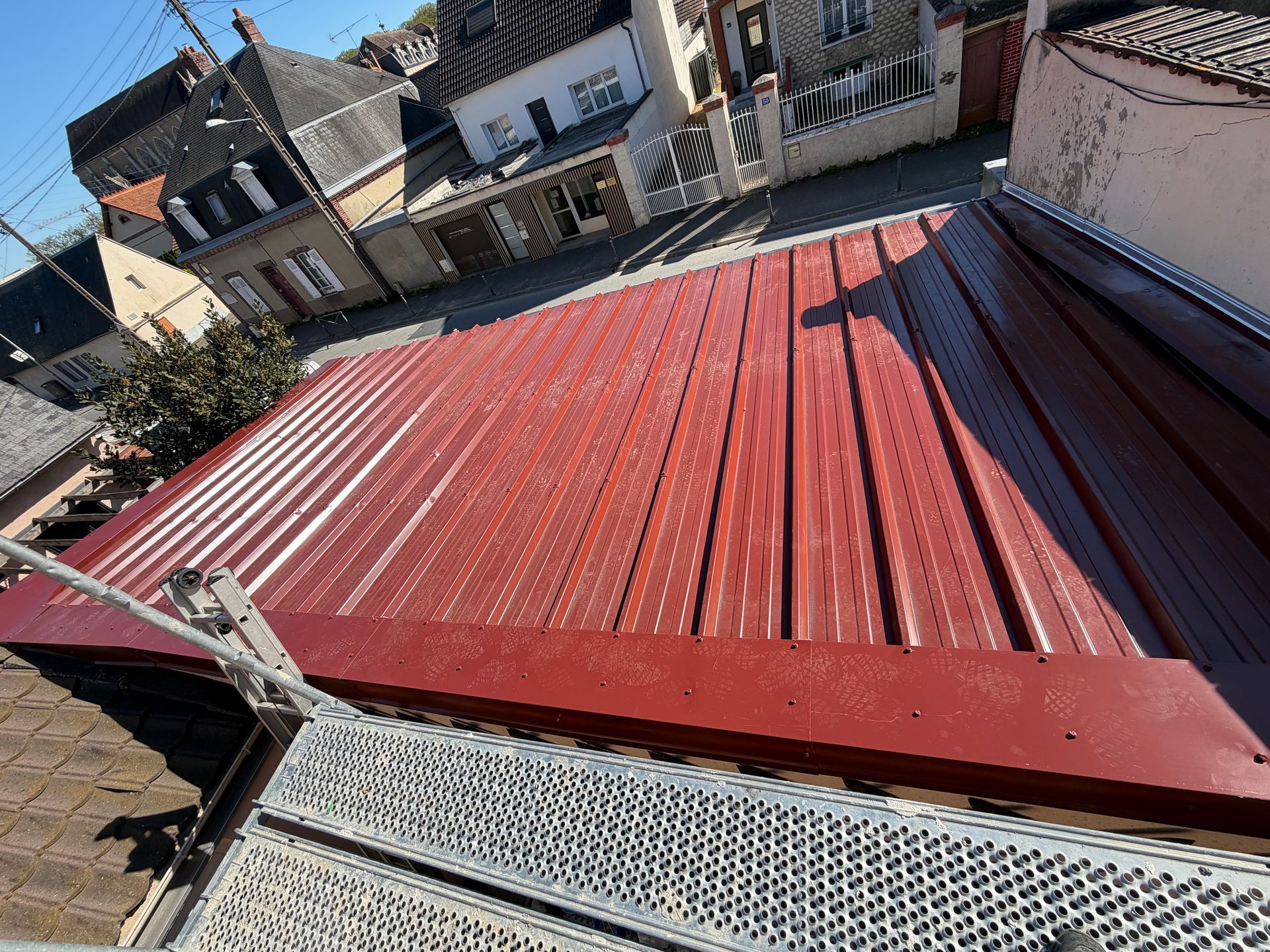 Toiture en tôle ondulée rouge sur une rangée de maisons, vue du ciel.