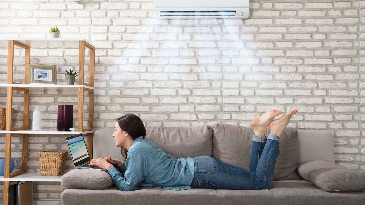 Mujer usando una computadora portátil en un sofá, con el aire acondicionado soplando aire fresco.