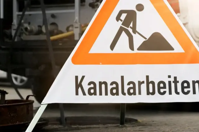 Orange-weißes Dreieckschild mit der Aufschrift „Kanalarbeiten“ warnt vor Bauarbeiten.