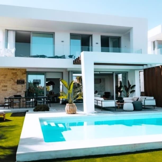 Villa moderna blanca con piscina turquesa y zona de estar al aire libre.
