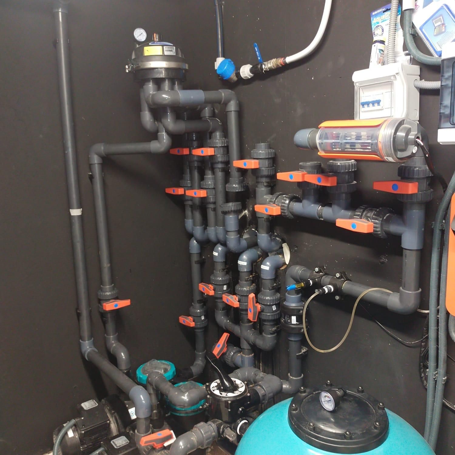 Equipos y tuberías de plomería interiores con válvulas naranjas y tanques azules en un cuarto de servicio.