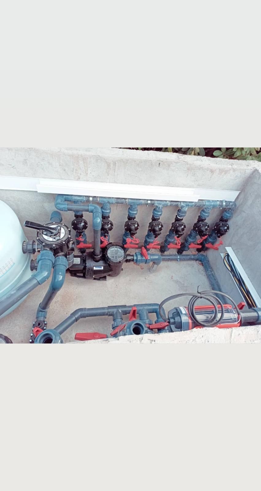 Tuberías y válvulas industriales dentro de una fosa de hormigón, con tuberías rojas y accesorios metálicos.