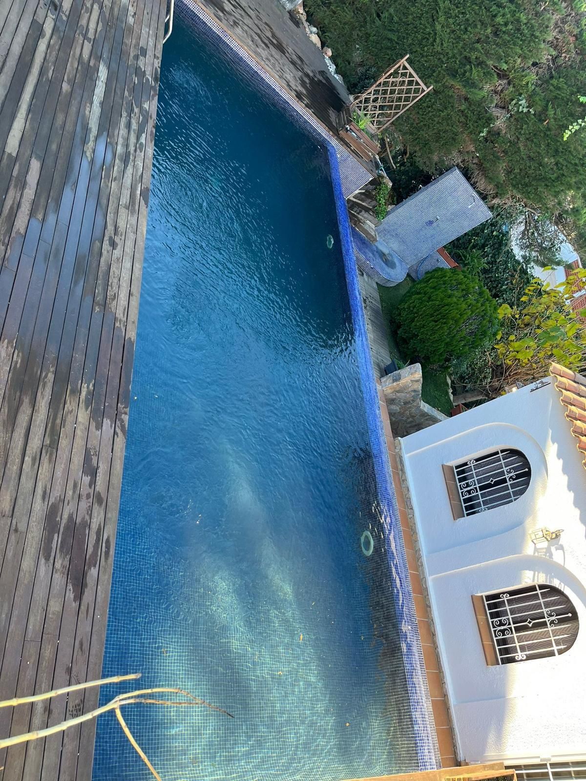 Piscina azul junto a una casa blanca y un patio de piedra, vista desde un ángulo al aire libre.