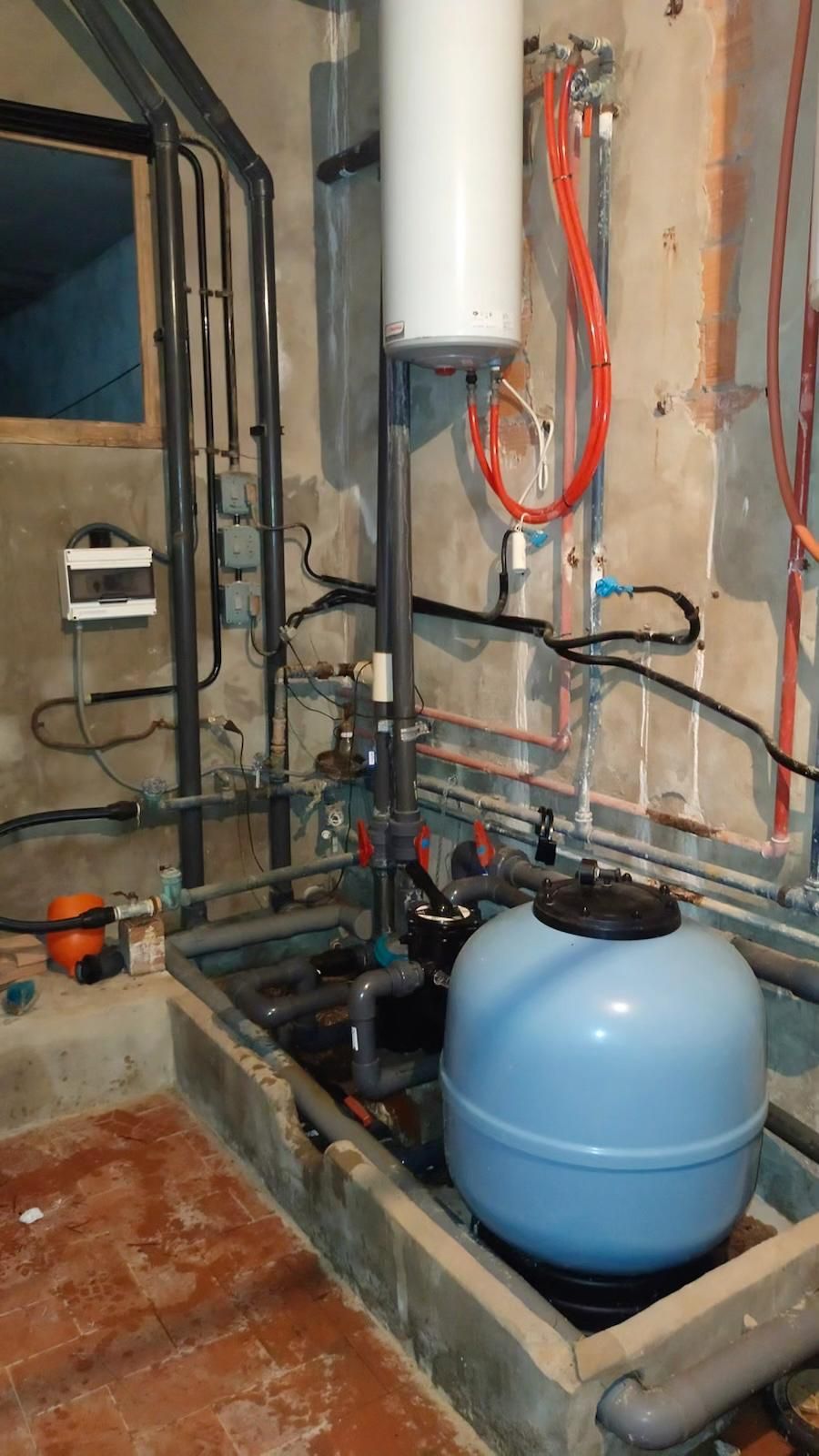 Área de servicio en el sótano con tuberías, un calentador de agua y un tanque de presión azul.