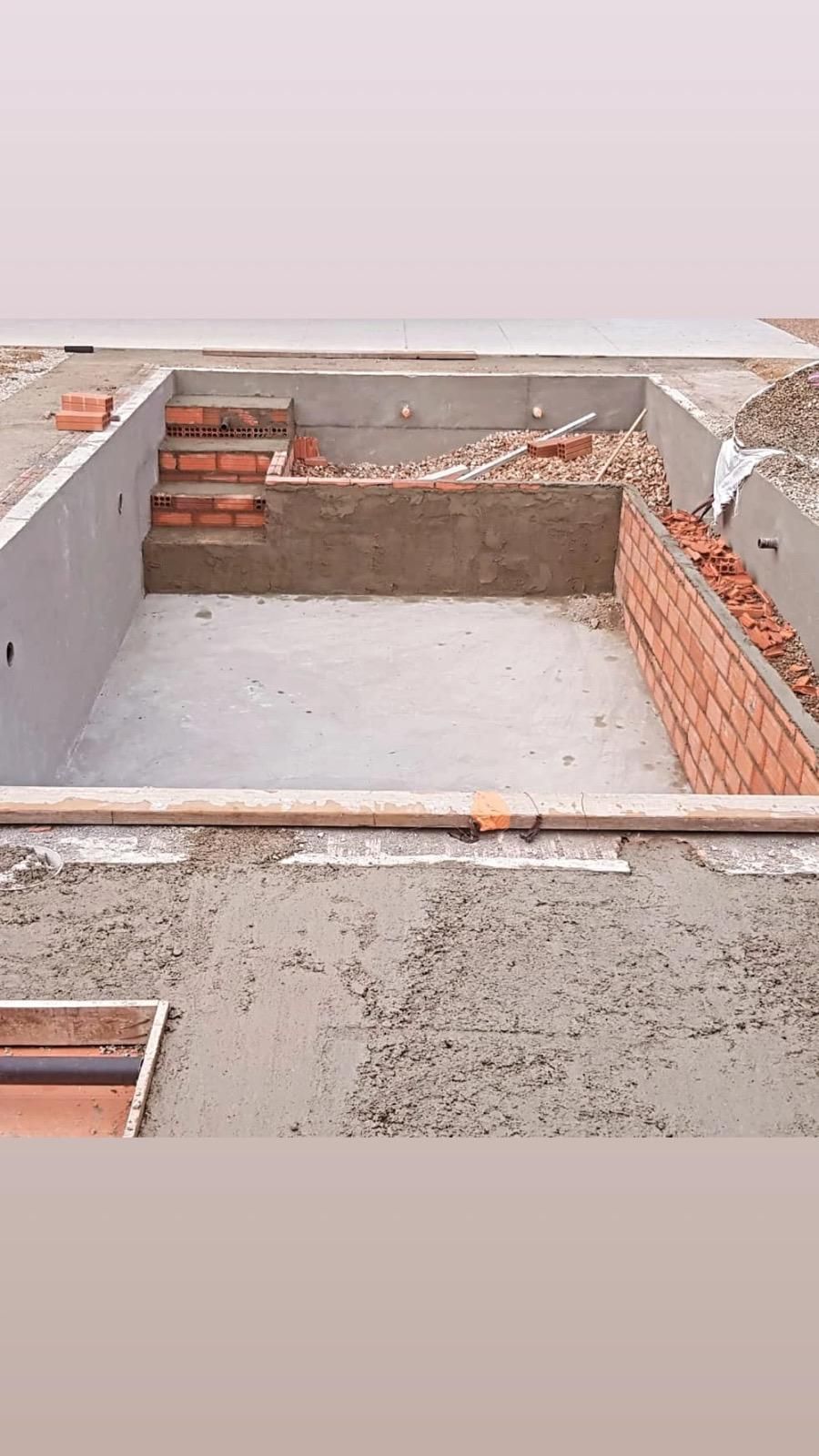 Habitación de hormigón sin terminar, con paredes de ladrillo rojo a la vista y escombros de construcción en el suelo.