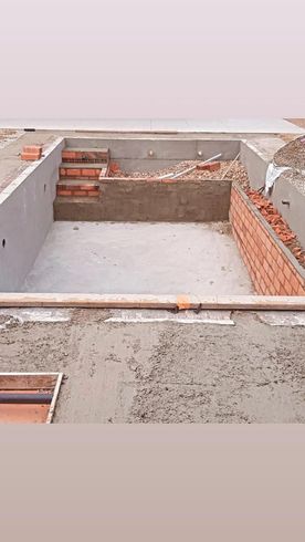Habitación de hormigón sin terminar, con paredes de ladrillo rojo a la vista y escombros de construcción en el suelo.