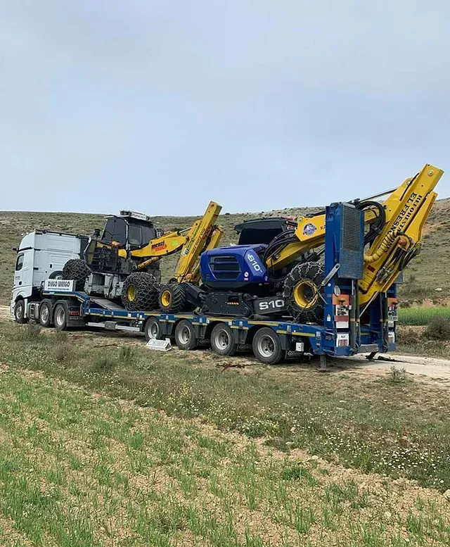 Un camión transporta un tractor en un remolque en un campo.