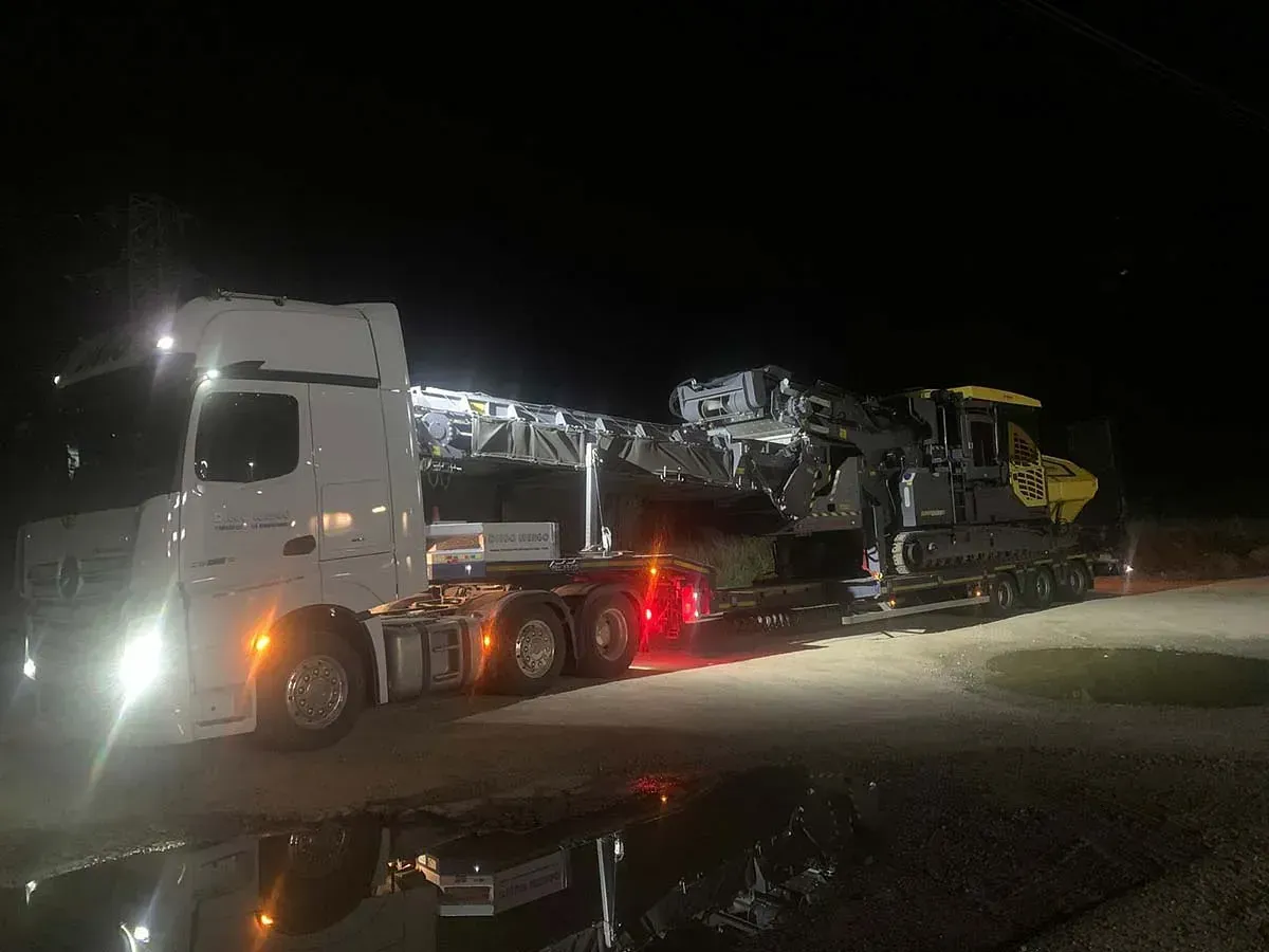 Un camión transporta una máquina grande en un remolque por la noche.