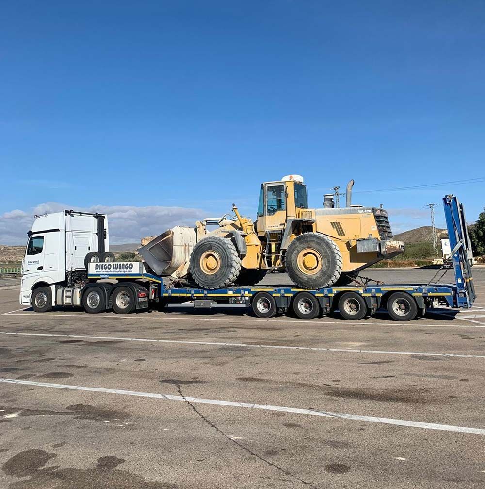 Un camión transporta una excavadora sobre un remolque en un estacionamiento.