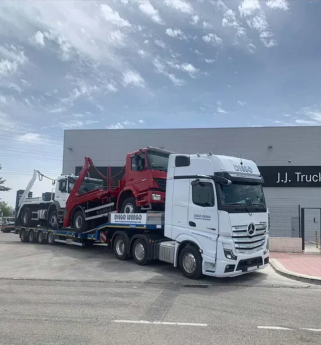 Un camión blanco transporta un camión rojo en un remolque.