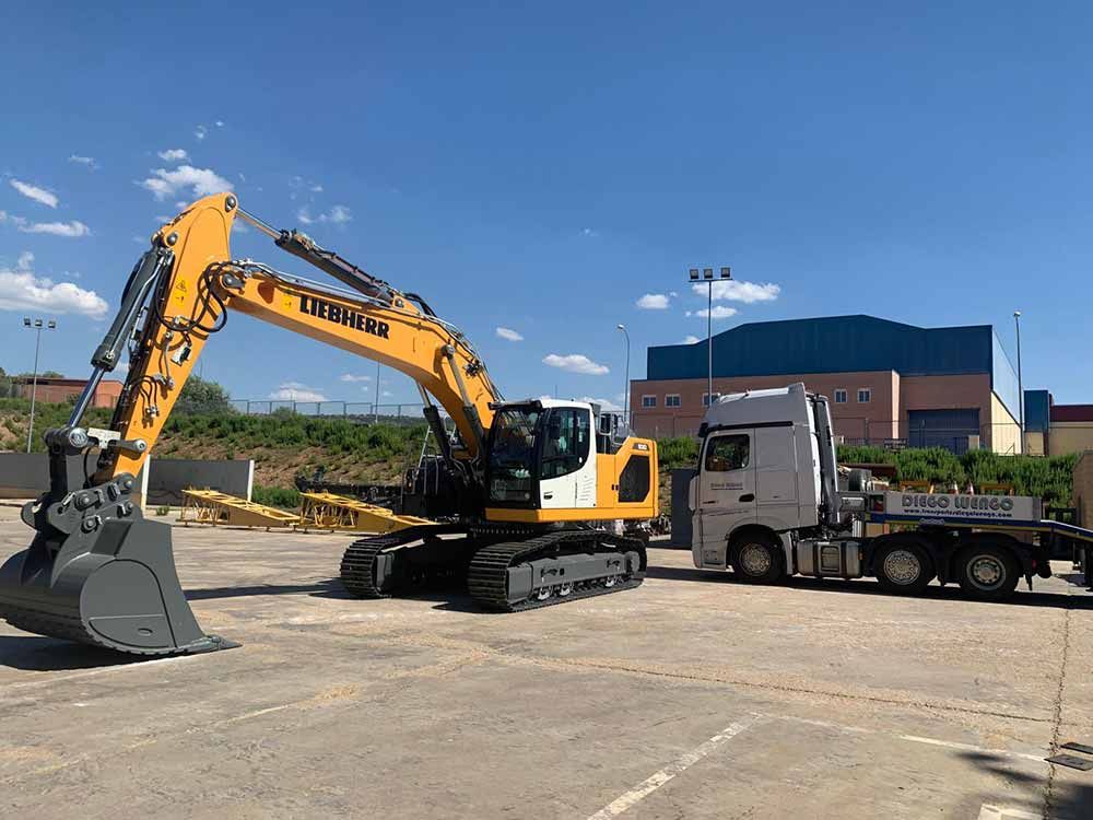 Una excavadora amarilla está estacionada junto a un camión en un estacionamiento.