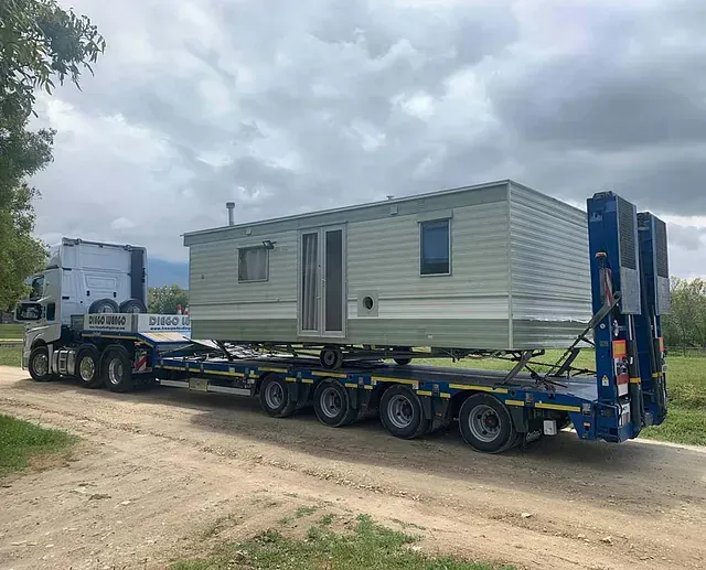 Una casa móvil está siendo transportada en un remolque por un camino de tierra.