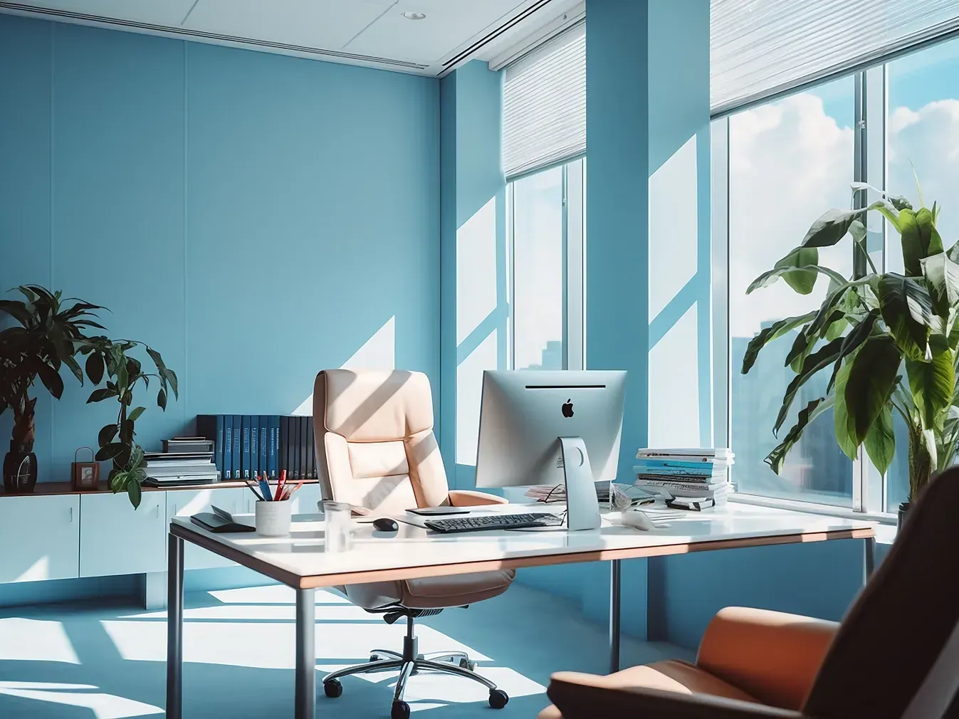 Oficina azul con escritorio, computadora, silla, plantas y ventana con luz solar.