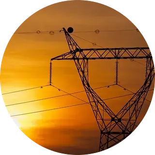Silueta de una torre de alta tensión contra un cielo de atardecer naranja y amarillo.