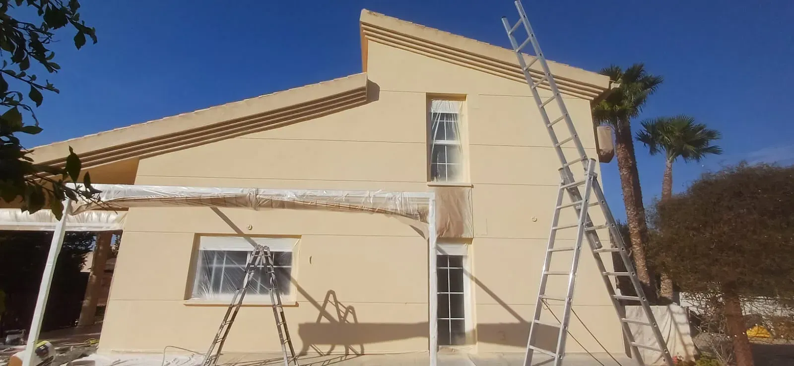Un edificio de color amarillo claro con una escalera alta apoyada contra él en un día soleado.