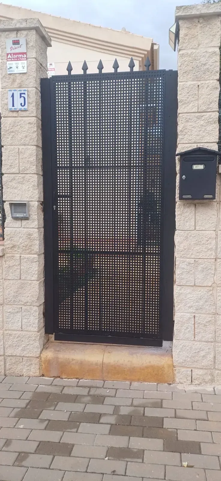 Puerta de metal negra en una entrada de muro de piedra, con dirección