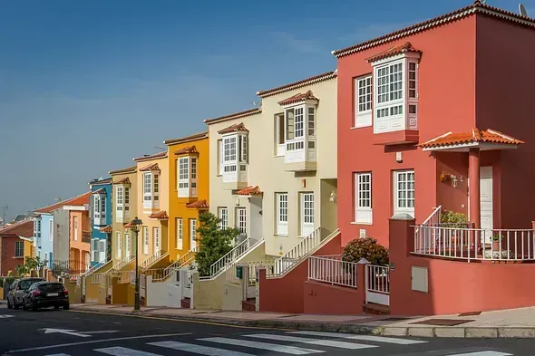 Casas adosadas de colores a lo largo de una calle con un paso de peatones y un coche.