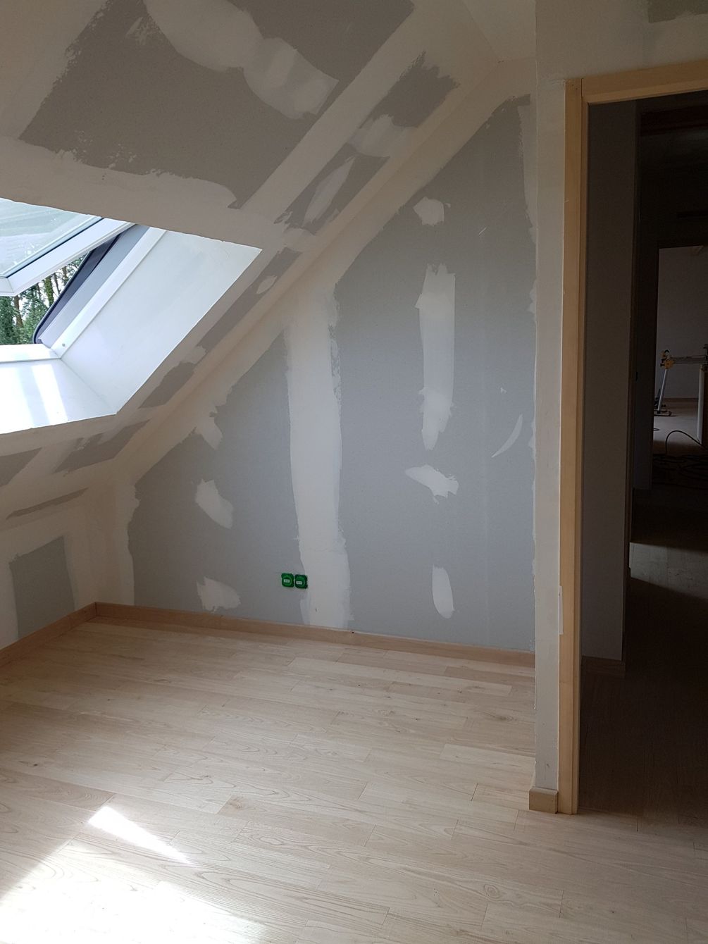 Petite pièce mansardée non aménagée avec puits de lumière, plafond mansardé, plaques de plâtre blanches et plancher en bois.