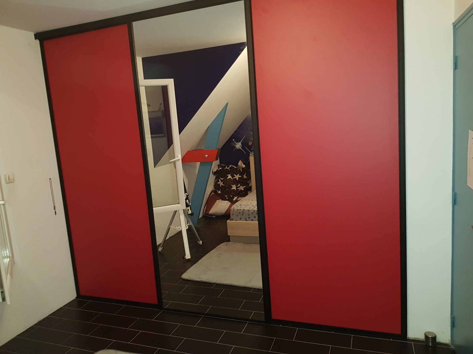 Aménagement intérieur Les portes coulissantes rouges du placard s'ouvrent partiellement sur une pièce contenant une échelle et des meubles.