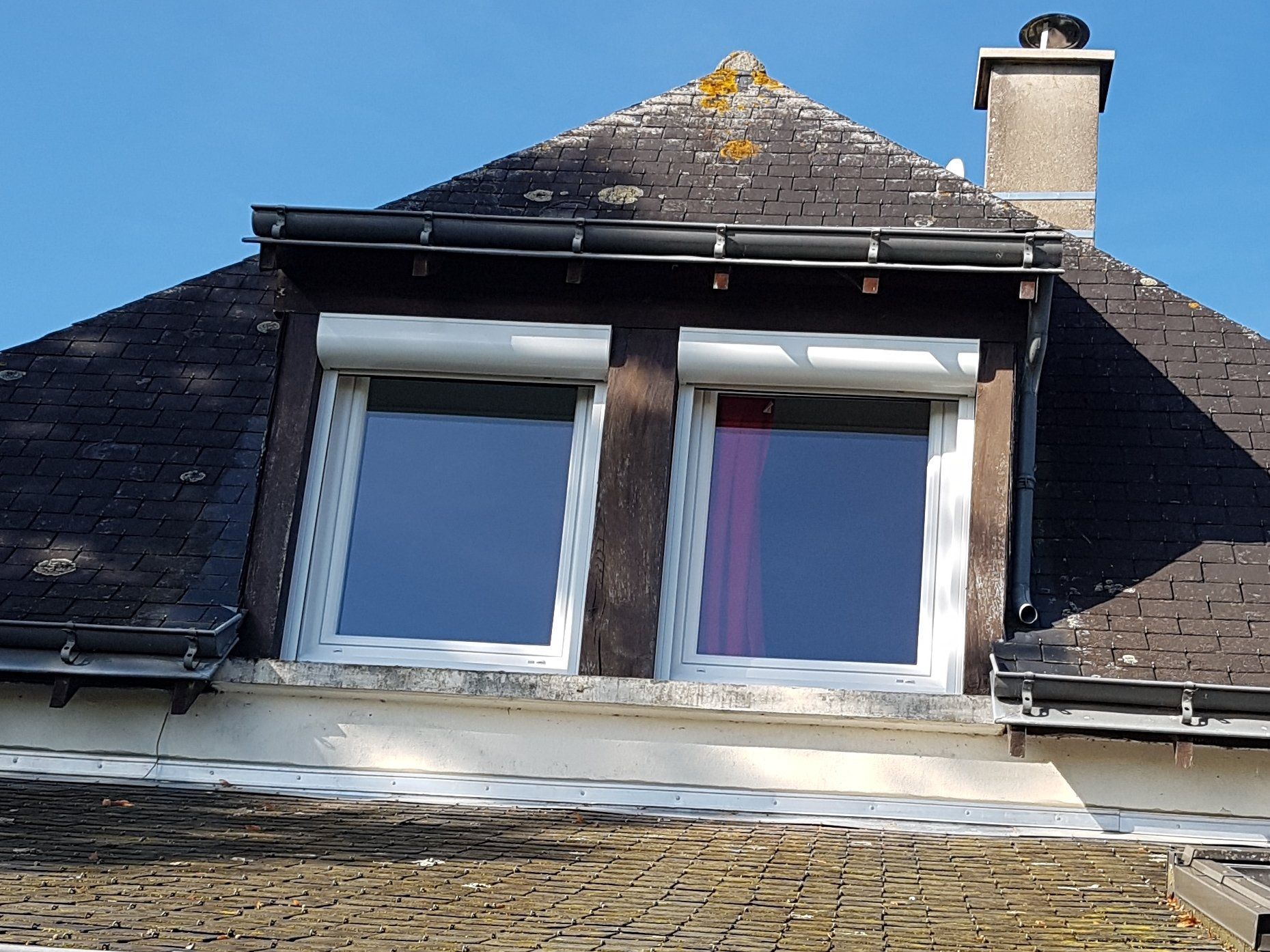 Isolation extérieure Lucarnes sur une maison au toit d'ardoise, avec une vitre cassée et une cheminée.
