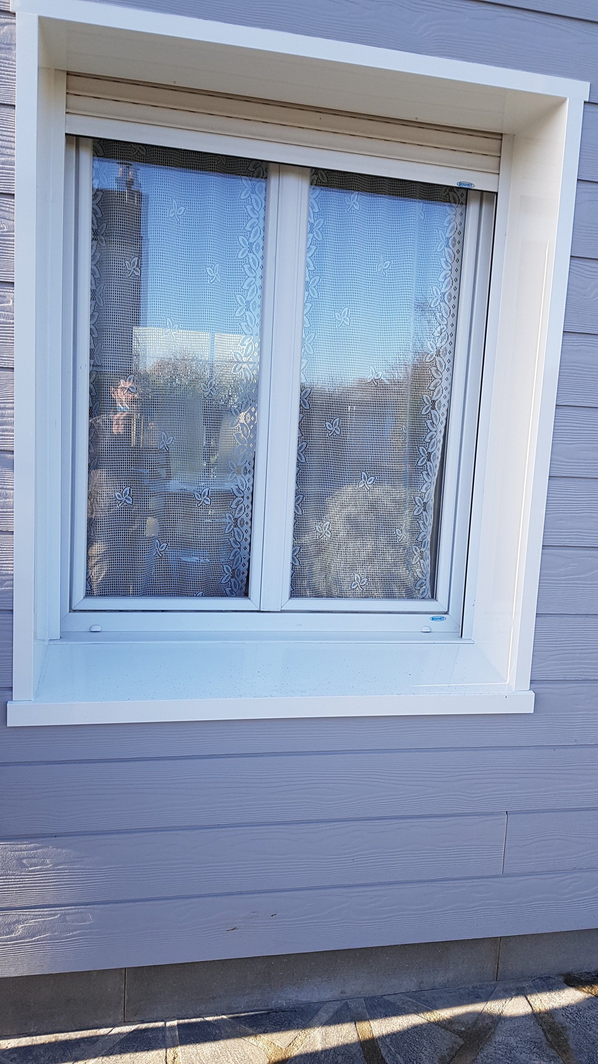 Fenêtre à cadre blanc avec rideaux à motifs sur une façade de maison gris clair