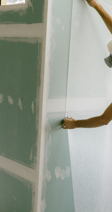 Une personne installant des plaques de plâtre tient une grande plaque contre un mur vert sur un chantier.