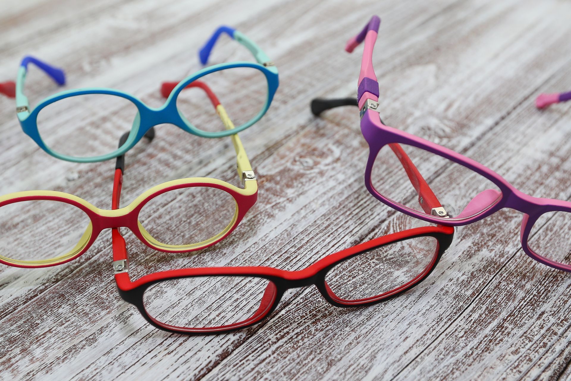 Des lunettes colorées éparpillées sur une surface en bois ; des montures de formes et de couleurs variées.