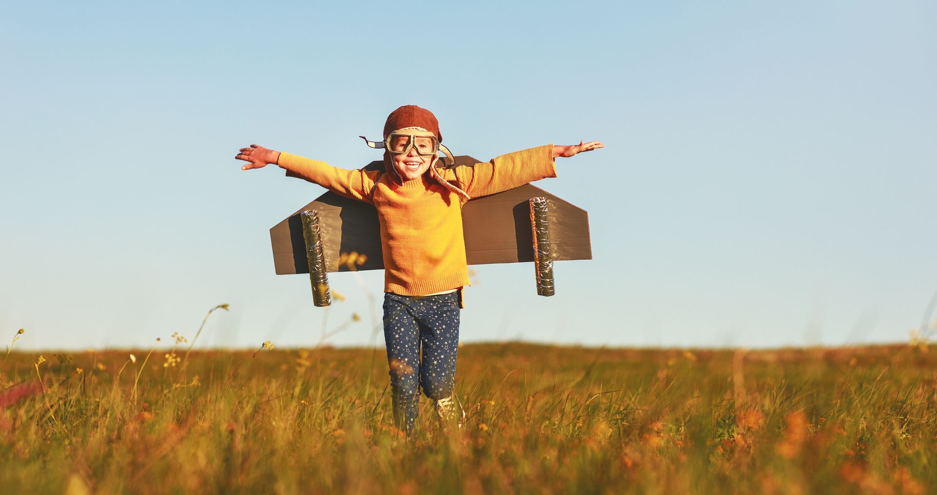 Enfant courant dans un champ avec un jetpack artisanal, les bras tendus, souriant.