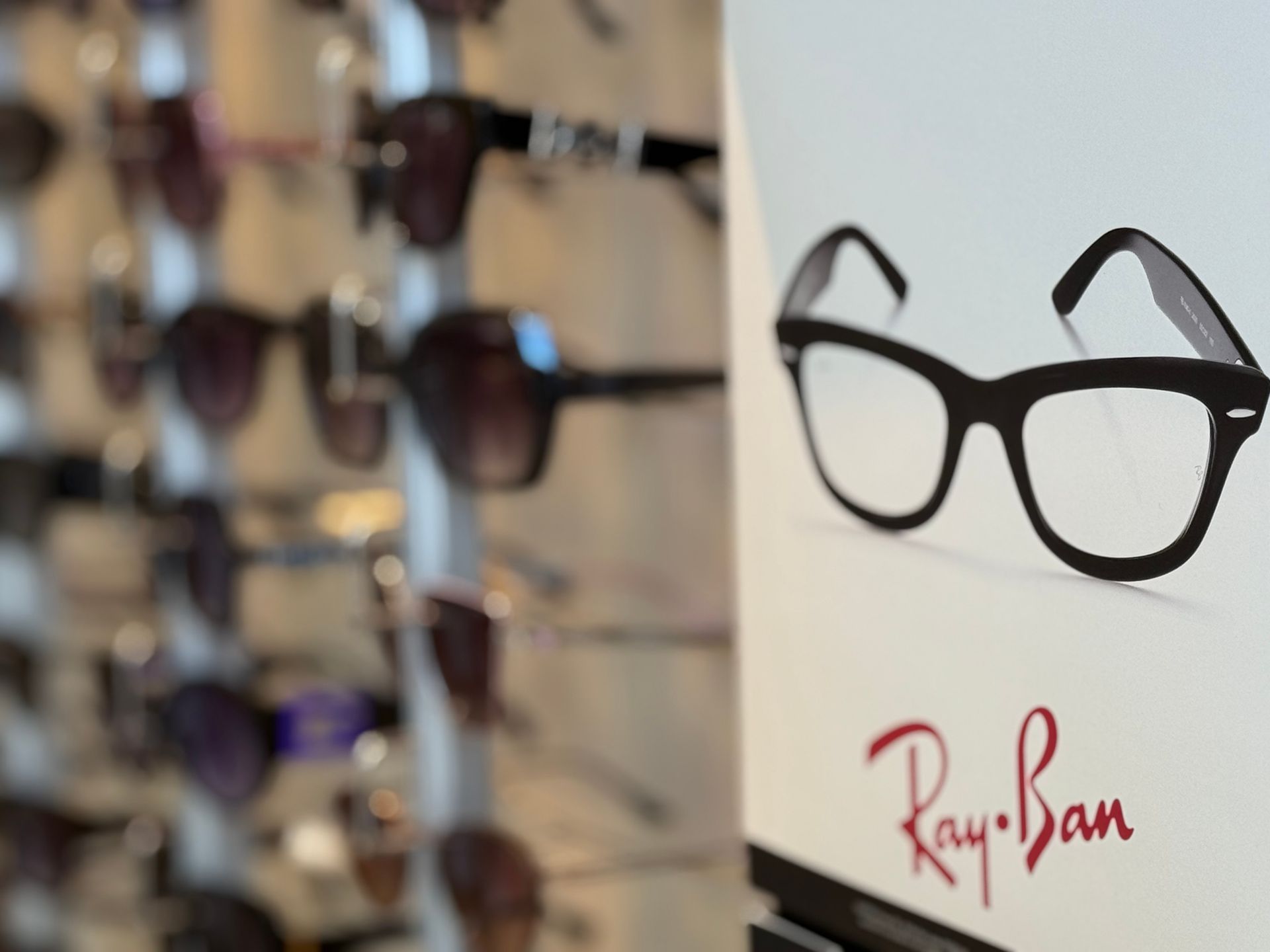 Publicité pour les lunettes Ray-Ban, avec des lunettes exposées en arrière-plan.