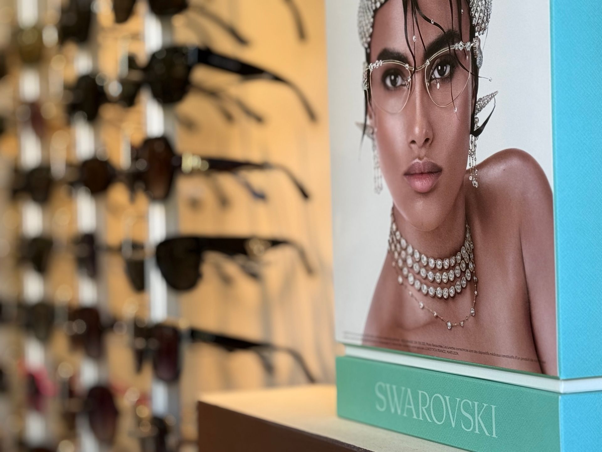 Des lunettes de soleil sont exposées, avec une publicité Swarovski mettant en scène une personne parée de bijoux.