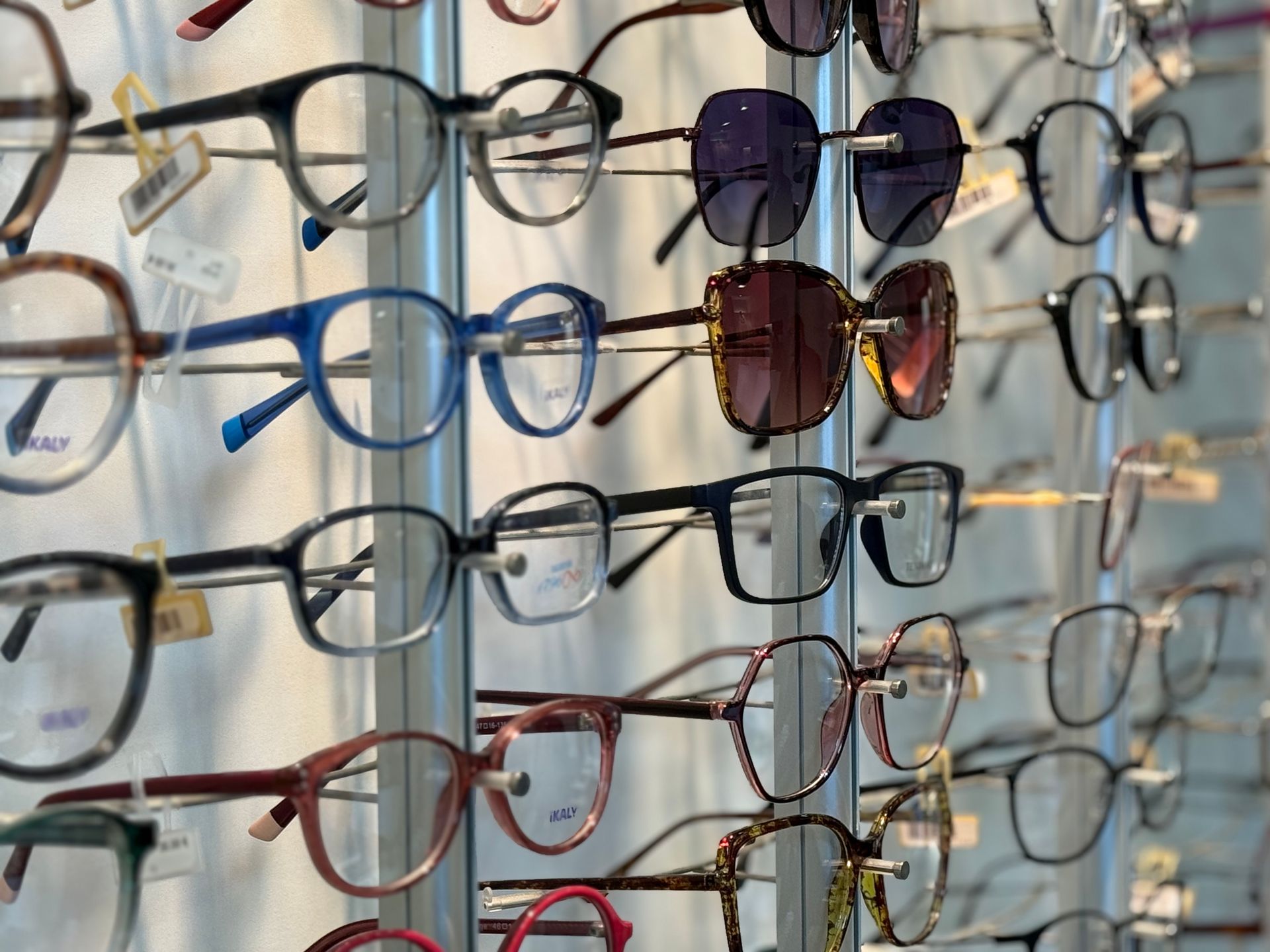 Des rangées de lunettes exposées dans un magasin, de styles et de couleurs de montures variés.