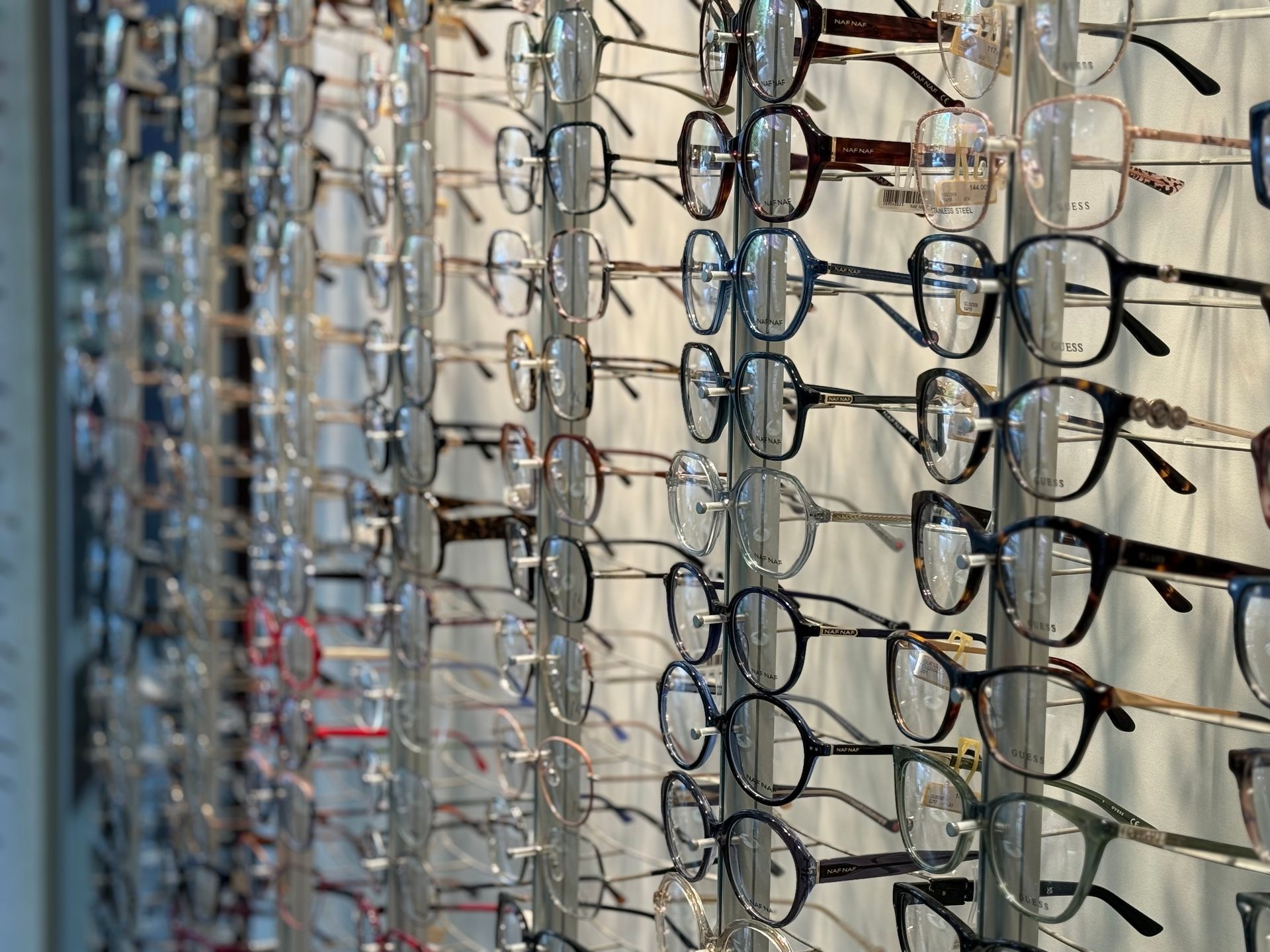 Des rangées de lunettes exposées sur un mur dans un magasin, beaucoup avec des montures noires ou transparentes.